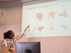The author, Rebecca, presenting her work, pointing to a slide entitled (Invisibility in Brussels)